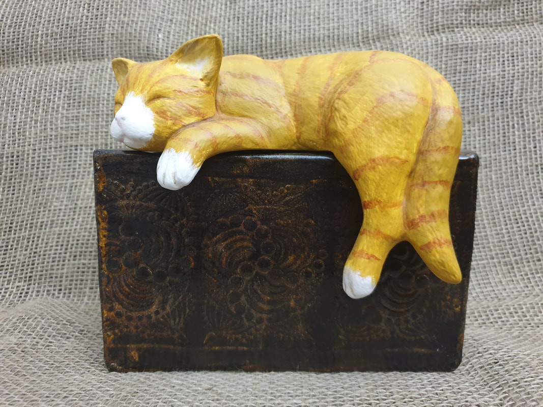 Ceramic Ginger Cat asleep and draped on a Bronze looking box